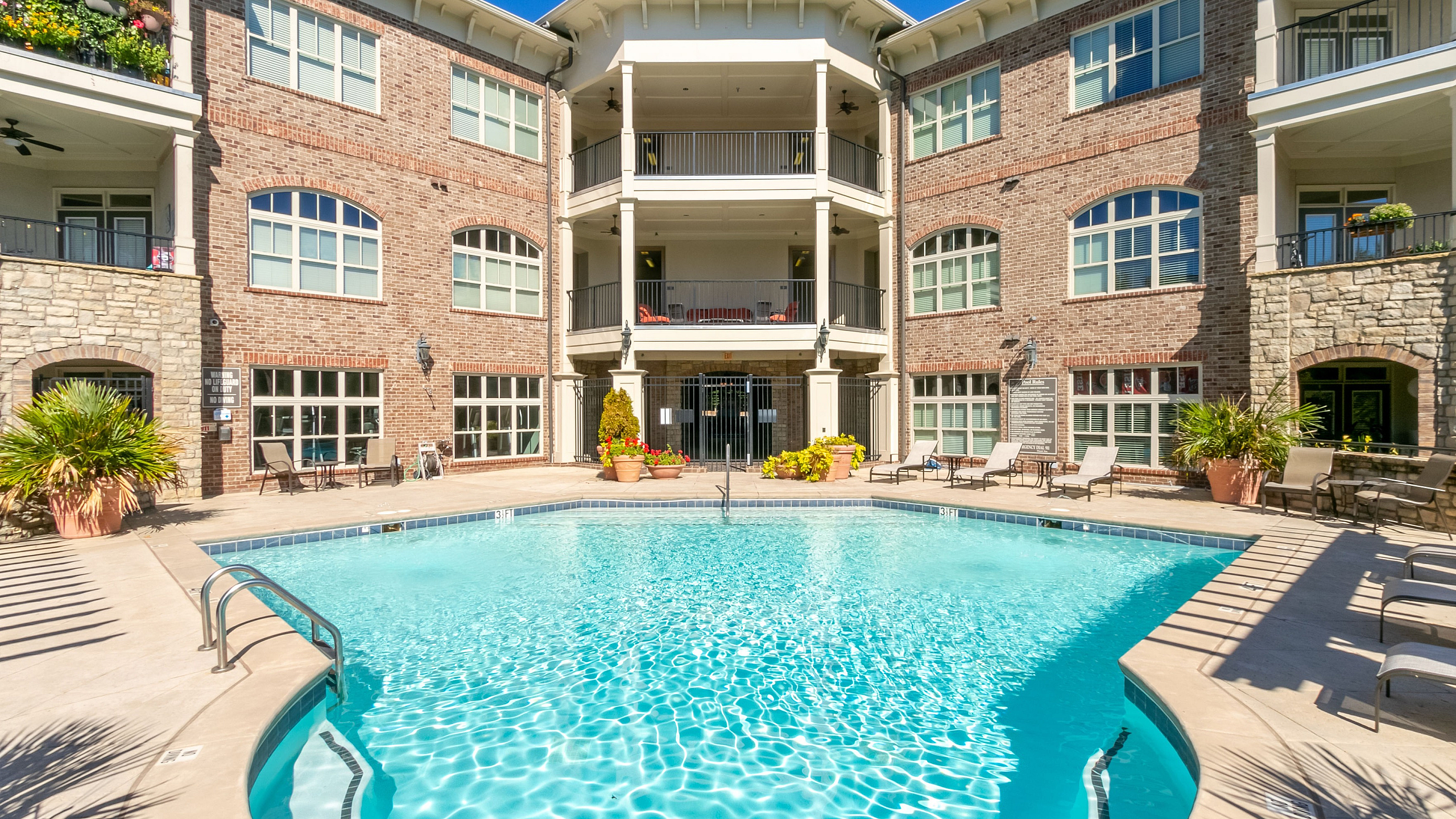 Elegant apartment complex with a stunning poolside view, featuring modern architecture and lush landscaping under a bright blue sky.
