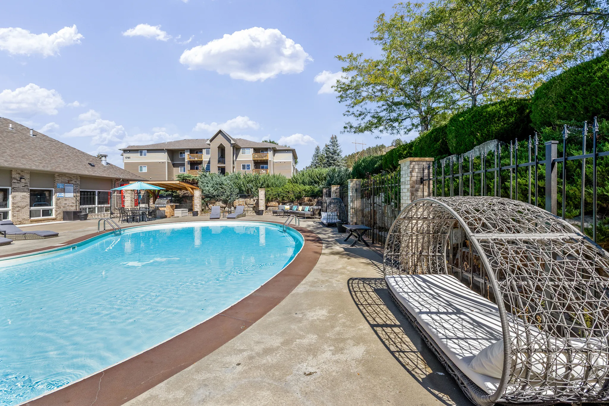 Inviting outdoor swimming pool area with modern lounge chairs and lush greenery, perfect for relaxation in a scenic apartment complex.
