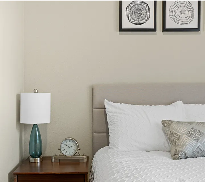 Inviting bedroom with plush white bedding, chic wooden nightstand, elegant table lamp, and modern art decor above the bed.