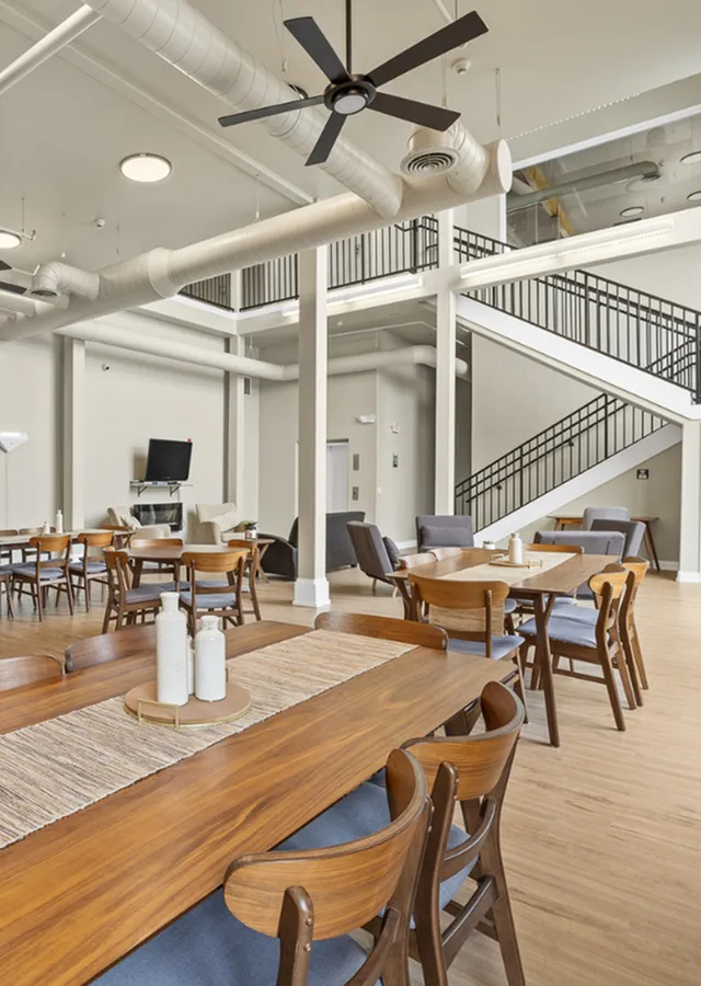 Modern communal space with elegant wooden dining tables, cozy seating, high ceilings, and industrial accents, perfect for social gatherings.