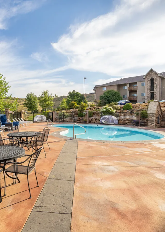 Inviting outdoor pool area with elegant seating, surrounded by lush greenery and a modern apartment building.