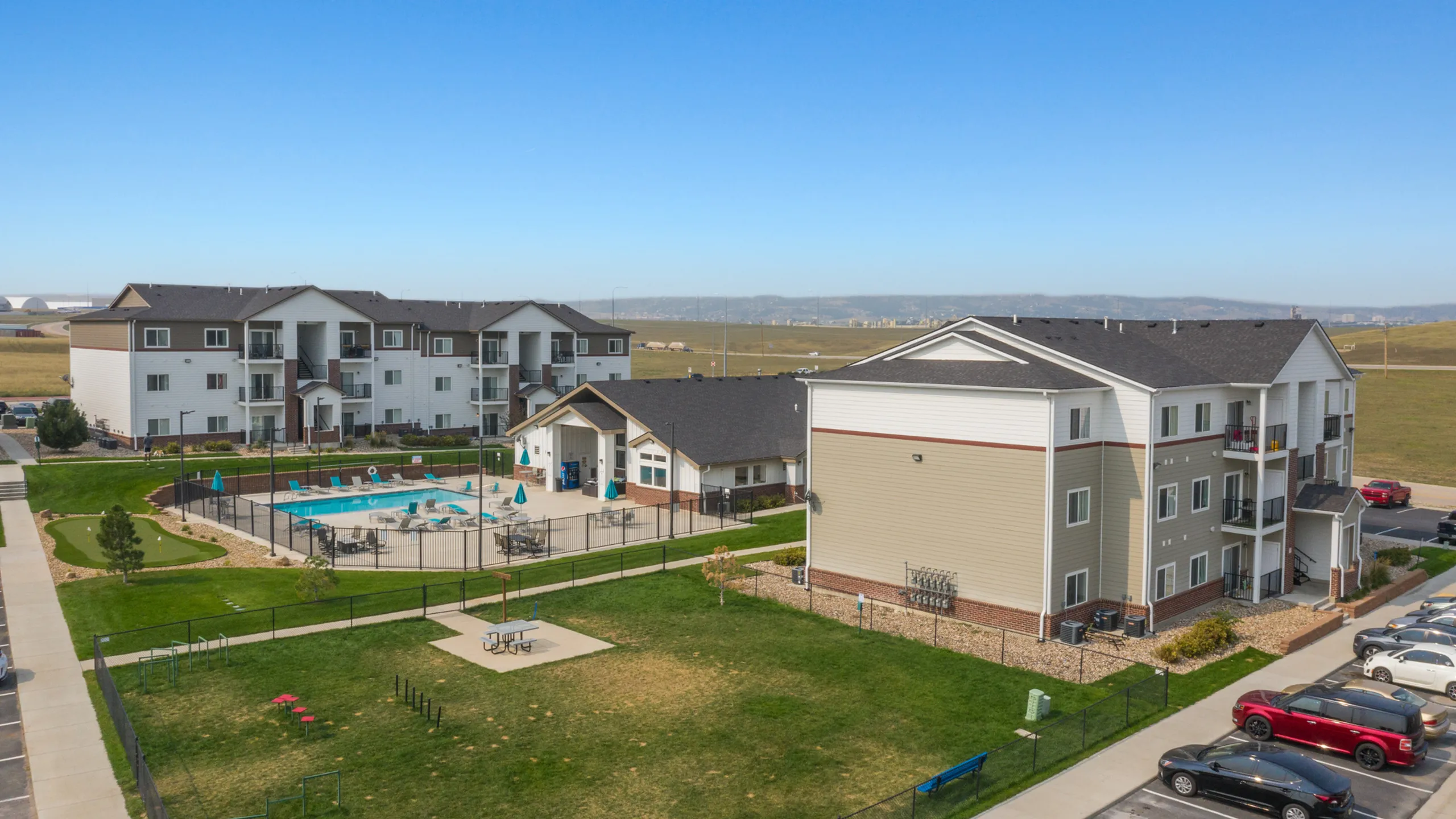 Modern apartment complex featuring a refreshing outdoor pool, well-maintained green spaces, and adjacent recreational areas set against a scenic backdrop.