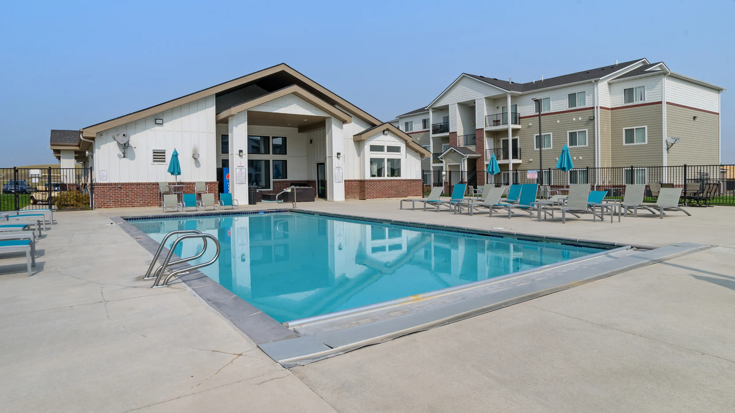 Inviting outdoor swimming pool area with modern sun loungers and a stylish clubhouse, perfect for relaxation and social gatherings.