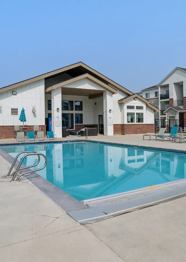 Inviting apartment complex with a pristine swimming pool, modern loungers, and a stylish clubhouse under a clear blue sky.