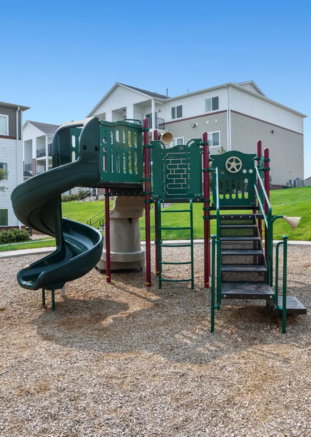 Inviting playground with a spiral slide and climbing structures, nestled next to modern apartment buildings with lush green lawns.
