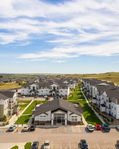 Charming aerial view of a modern apartment community with neatly arranged buildings and lush green spaces, set against a picturesque sky.