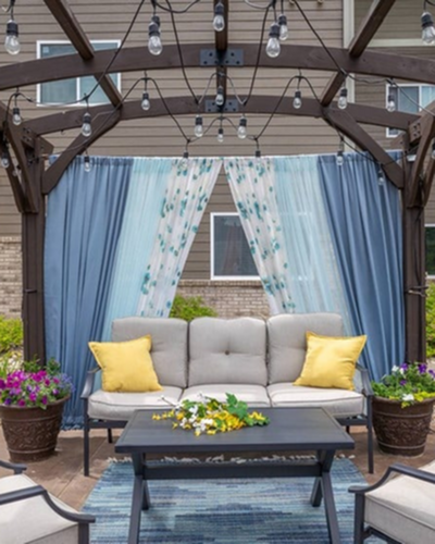 Charming outdoor seating area under a wooden pergola with cozy cushions and vibrant hanging lights.