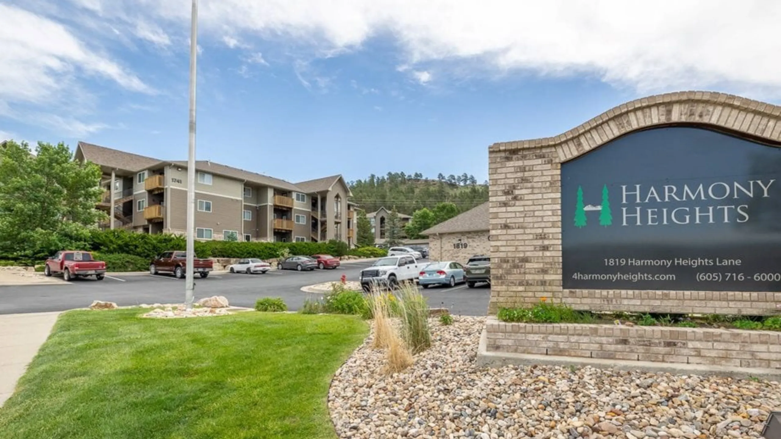 Charming Harmony Heights apartment complex with inviting greenery and ample parking under a bright blue sky.