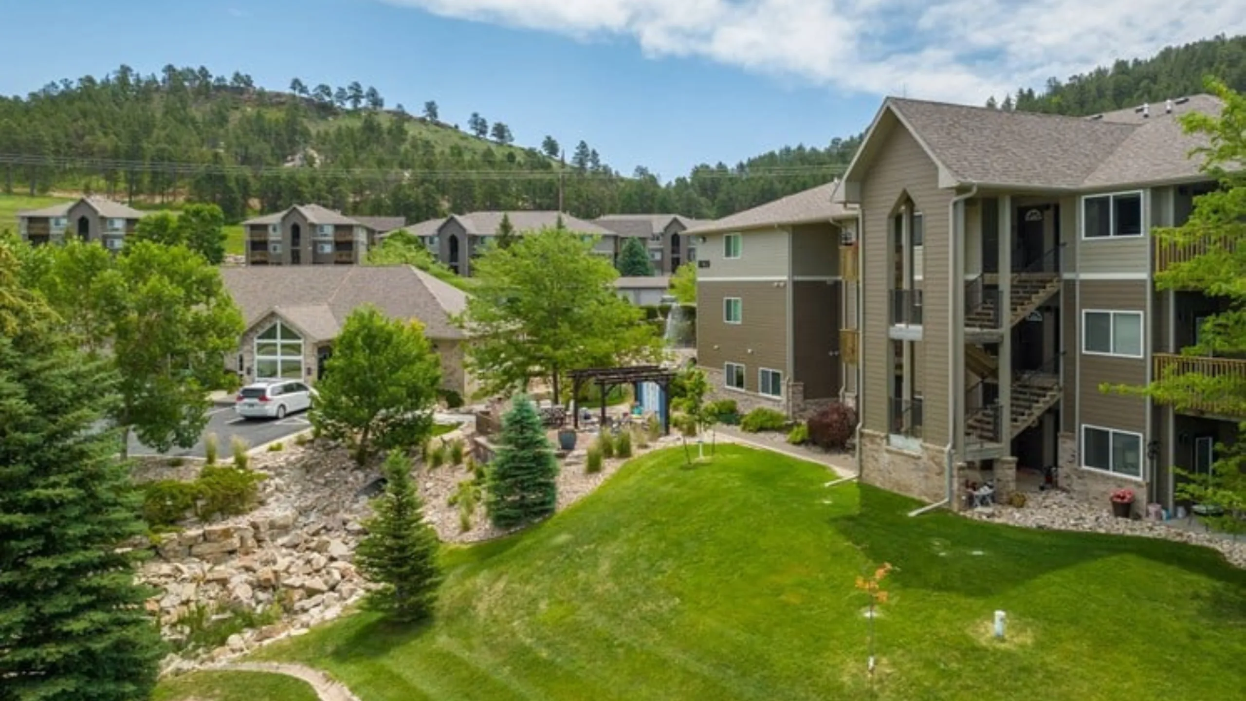 Scenic apartment complex with modern architecture, surrounded by lush greenery and picturesque hills.