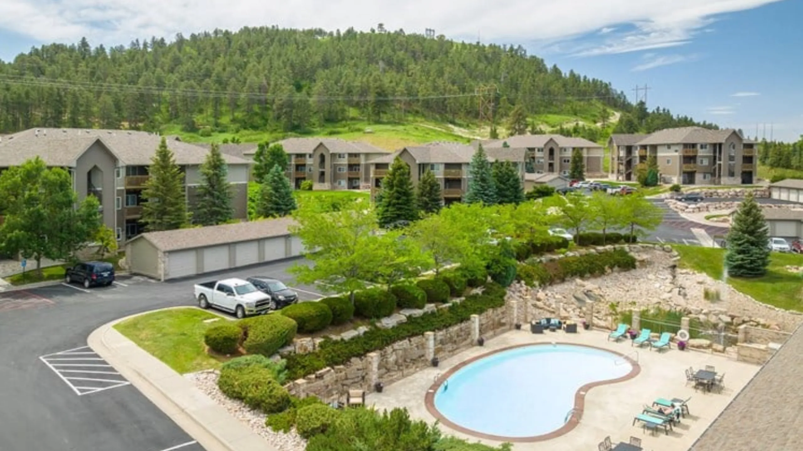 Scenic apartment complex nestled among lush greenery with a refreshing outdoor pool and comfortable lounging area.