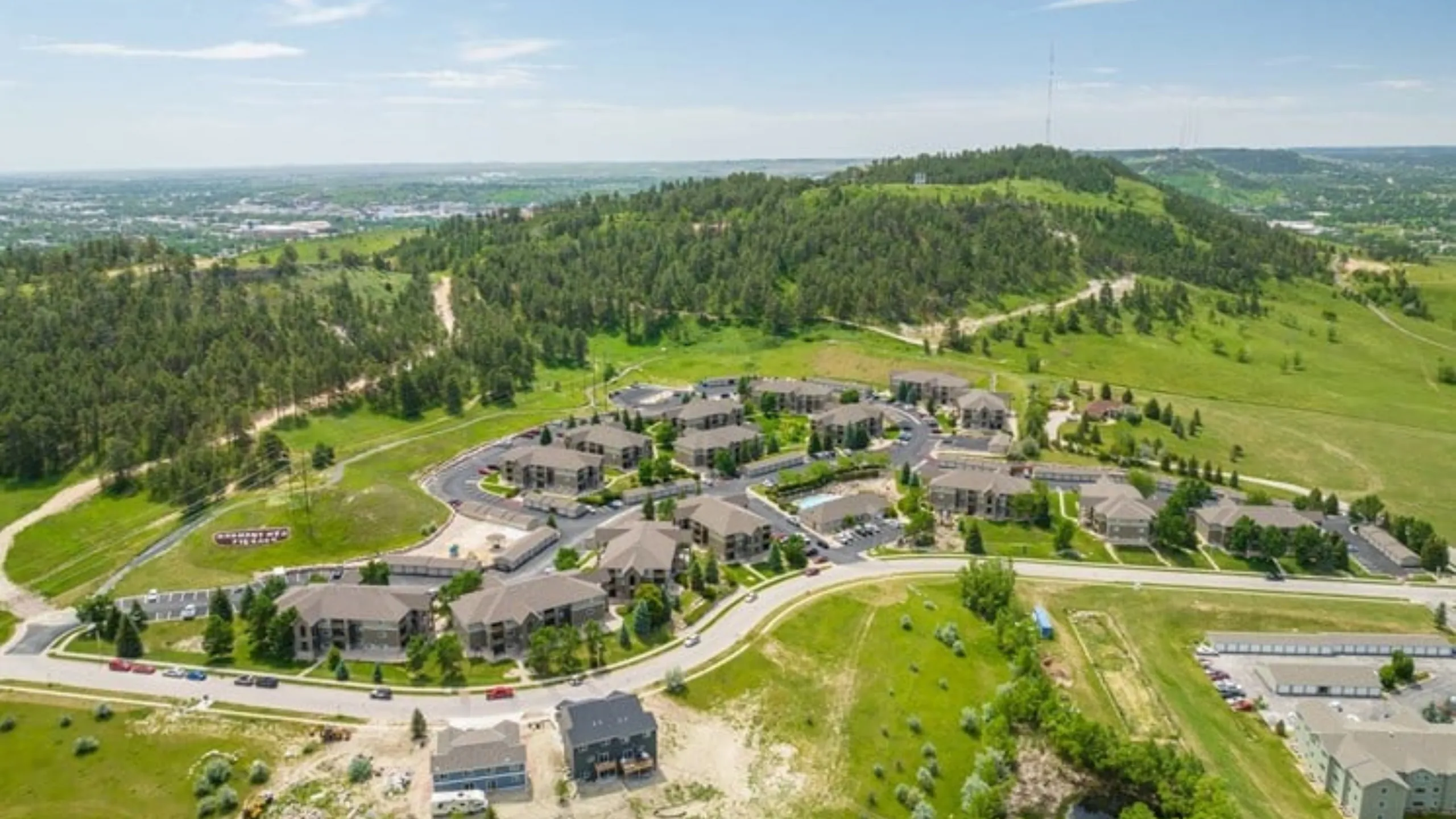 Aerial view of a modern apartment complex nestled in lush green hills, offering stunning landscape views and ample open space.