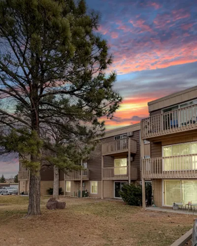 Charming apartment building with private balconies set against a vibrant sunset sky, surrounded by lush trees.