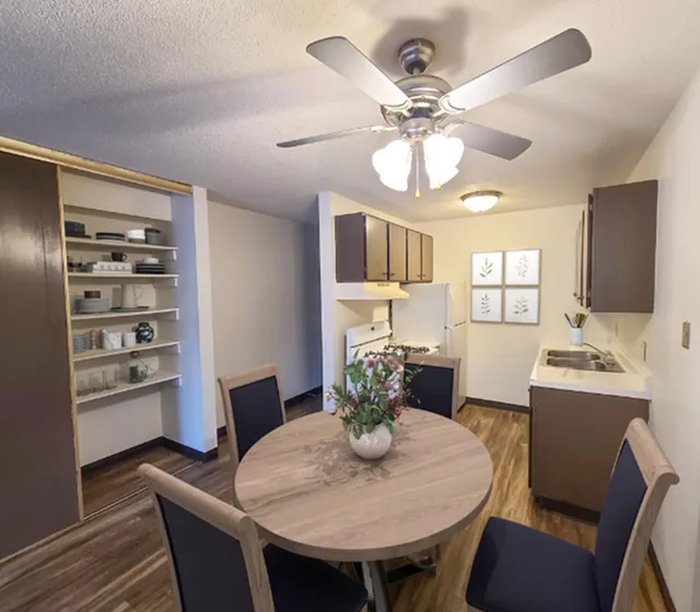Cozy dining area with modern amenities, featuring a round wooden table, elegant ceiling fan, and contemporary kitchen setup with open shelving and stylish decor.