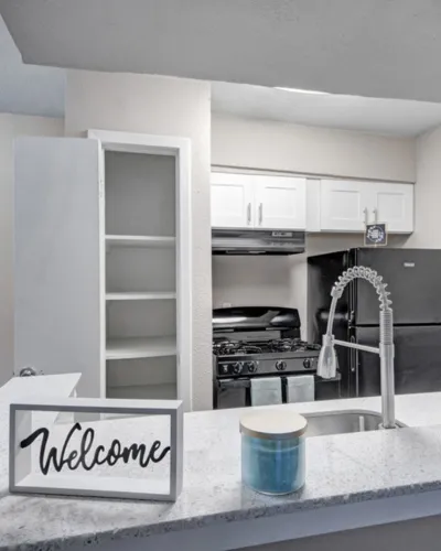 Inviting modern kitchen with sleek stainless steel appliances, pristine white cabinets, and a cozy welcome sign on the countertop.