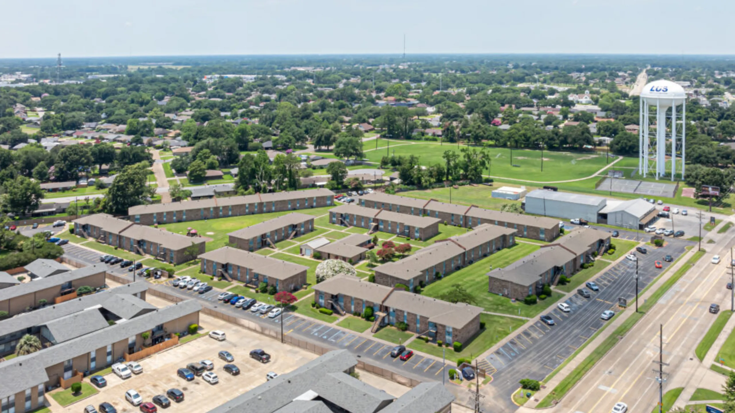 Expansive aerial view of a charming apartment complex with lush green spaces, ample parking, and a vibrant community atmosphere.