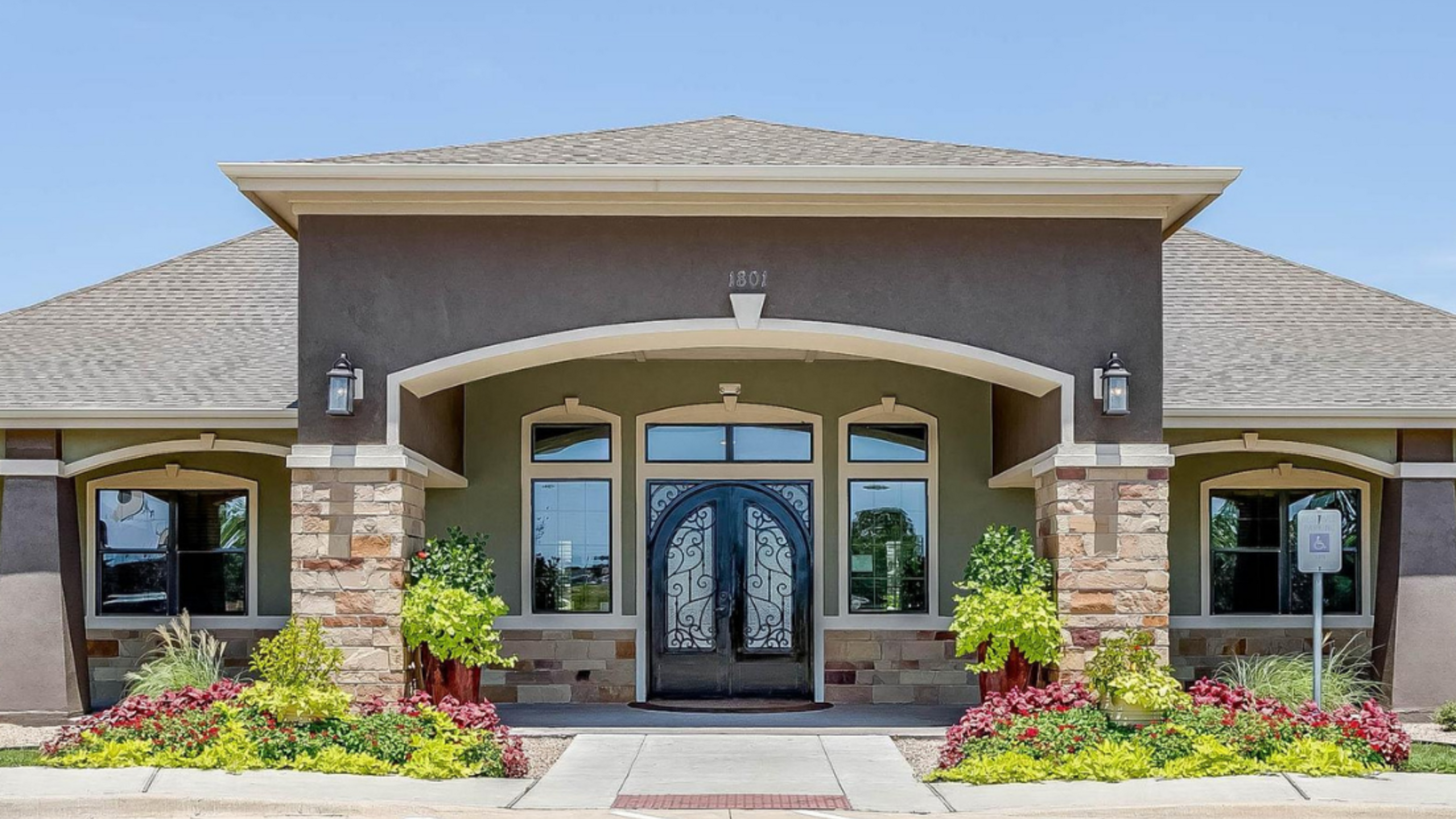 Charming apartment entrance showcasing elegant arched windows, decorative wrought iron doors, and vibrant landscaping.
