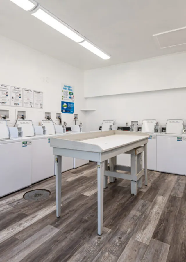 Bright and spacious laundry room featuring modern washing machines and a central folding table on sleek wood flooring.