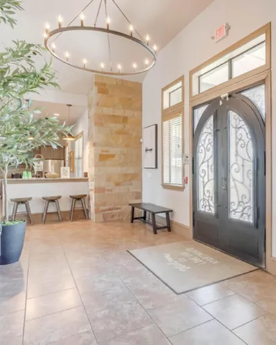 Inviting apartment entryway with elegant chandelier, stylish arched doors, and cozy seating area next to a modern kitchen counter.