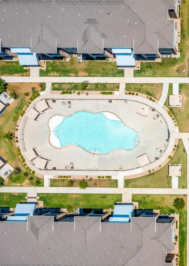 Aerial view of a luxurious apartment complex featuring a stunning, resort-style swimming pool surrounded by elegant sun loungers and beautifully landscaped grounds.