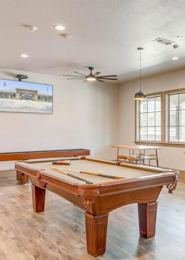 Elegant game room featuring a classic pool table with cues and balls, stylish ceiling fan, large windows for natural light, and chic pendant lighting.