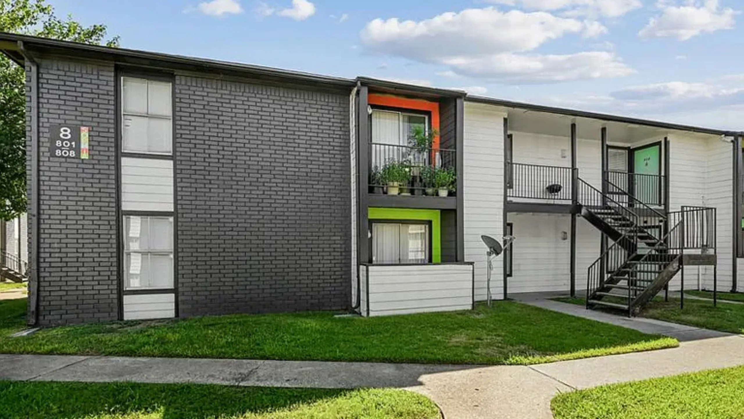 Modern apartment exterior with vibrant accents and private balconies, surrounded by lush green lawns and clear blue skies.