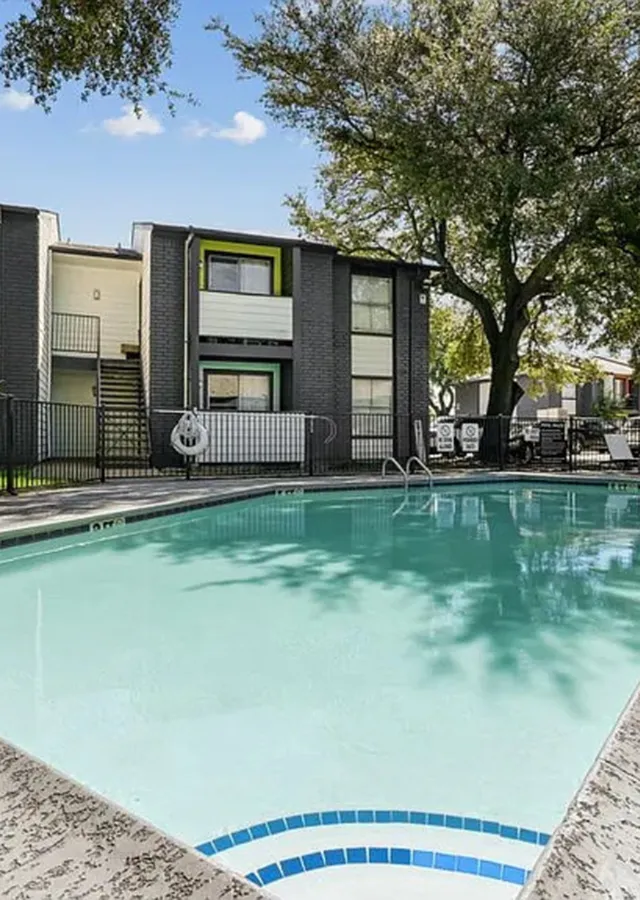 Inviting apartment complex with a sparkling swimming pool and charming outdoor seating area surrounded by lush greenery.