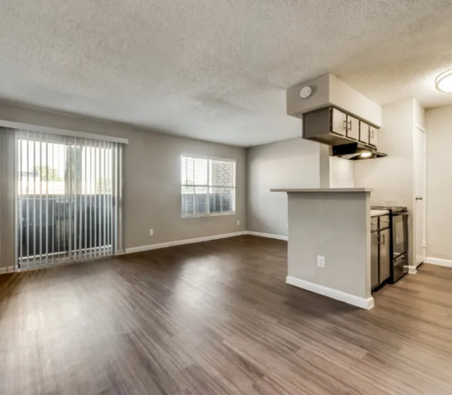 Modern open-concept living space featuring sleek wooden flooring, large windows, and a contemporary kitchen with stainless steel appliances.