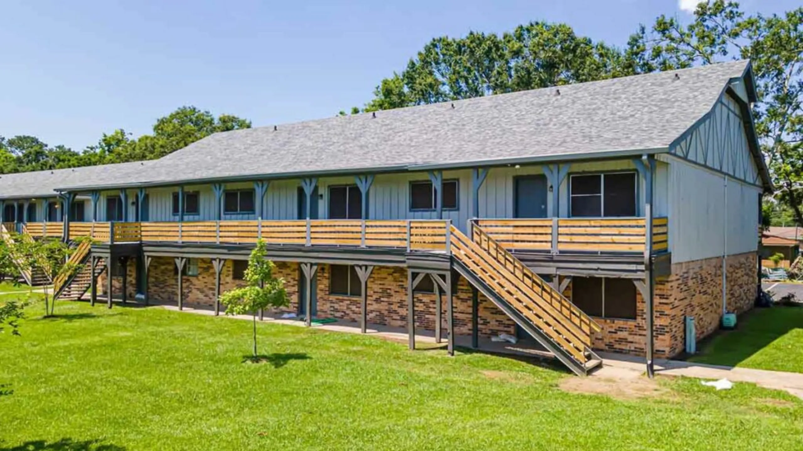 Charming multi-unit apartment building with rustic brick accents, surrounded by lush greenery and inviting wooden staircases.