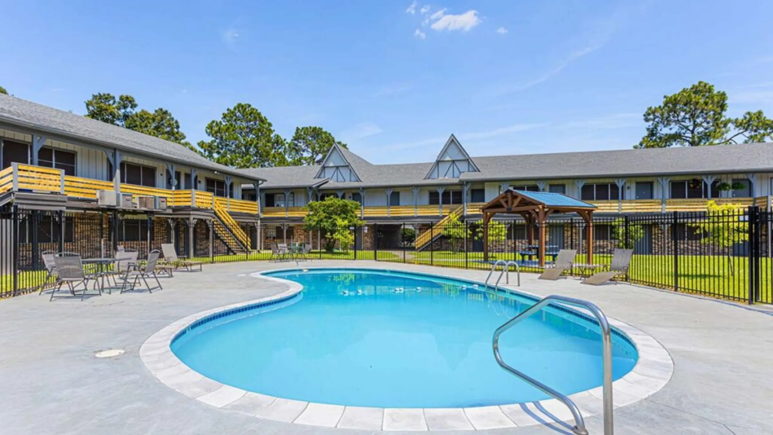 Inviting courtyard with a sparkling swimming pool, surrounded by charming two-story apartments and lush greenery.