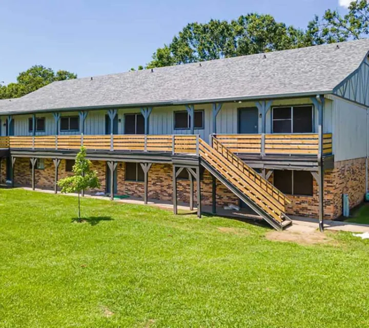 Inviting two-story apartment building with charming wooden balconies and a lush green lawn, perfect for serene living.