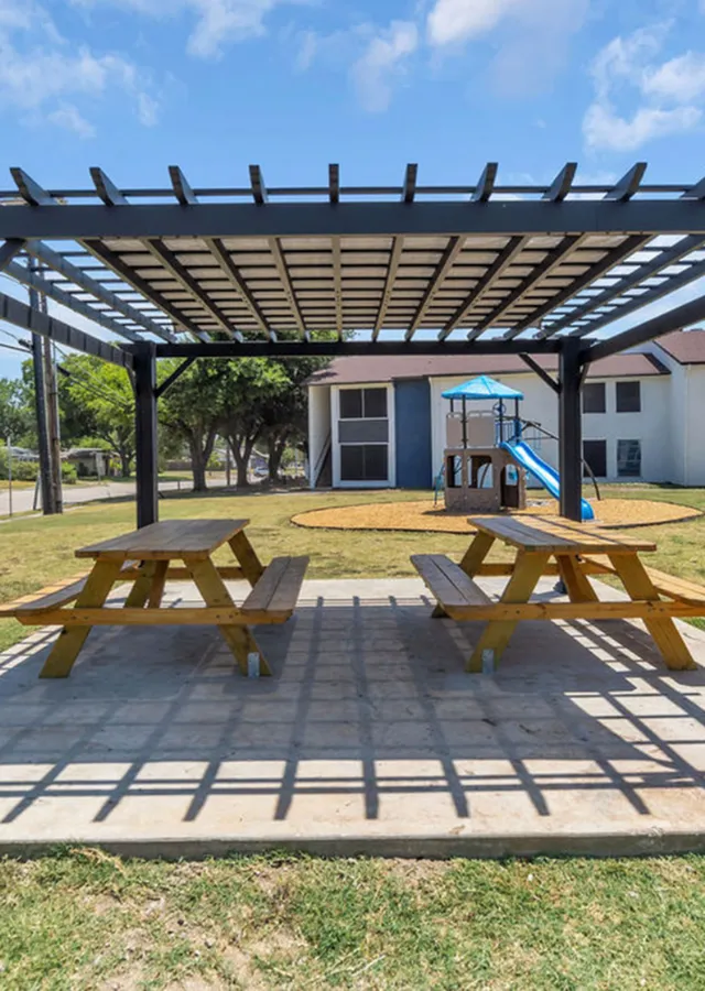 Inviting outdoor space featuring a pergola with picnic tables and a vibrant playground, perfect for family gatherings.
