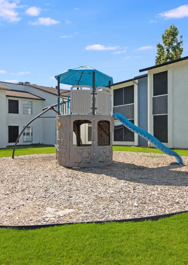 Charming apartment playground featuring a modern play structure with a slide, surrounded by lush green grass, perfect for family enjoyment.