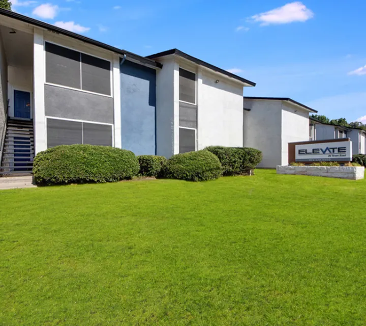 Inviting exterior view of a modern apartment complex with lush green landscaping and a welcoming signage reading 'Elevate'.