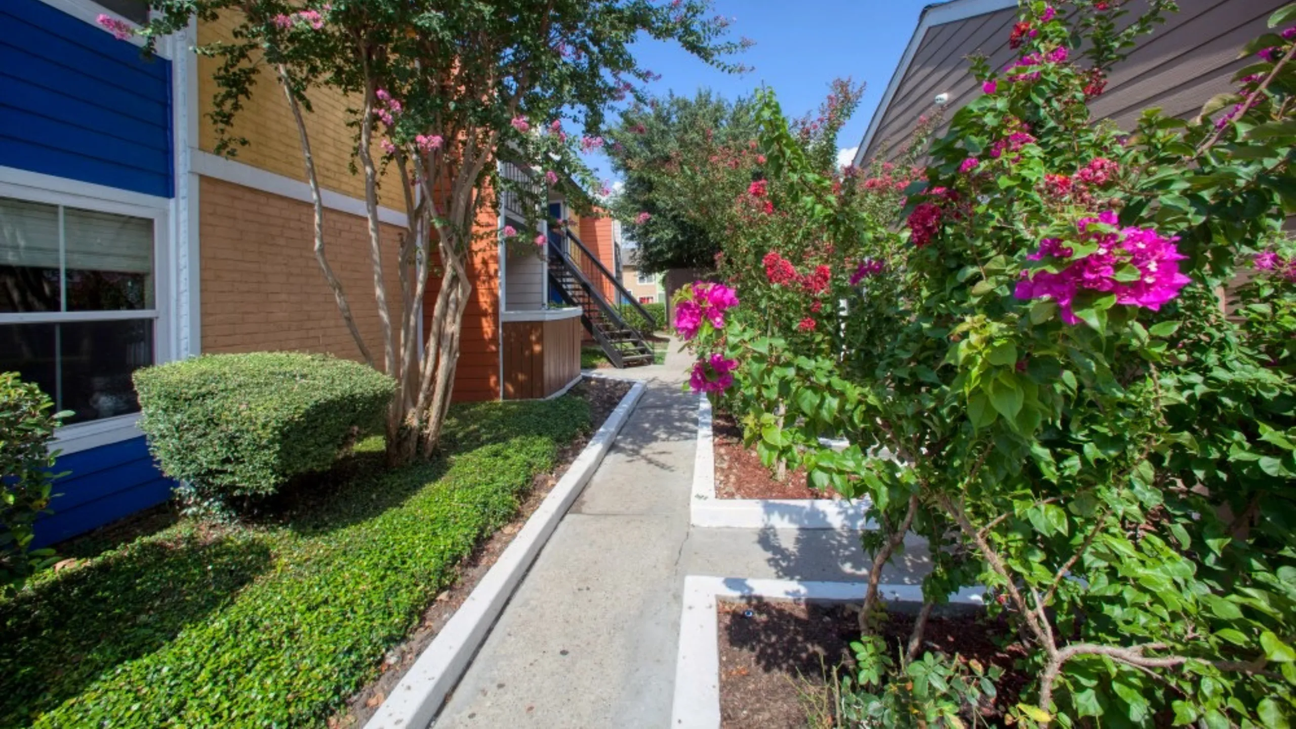 Vibrant apartment walkway adorned with lush greenery and blooming flowers, creating a welcoming and serene entrance.