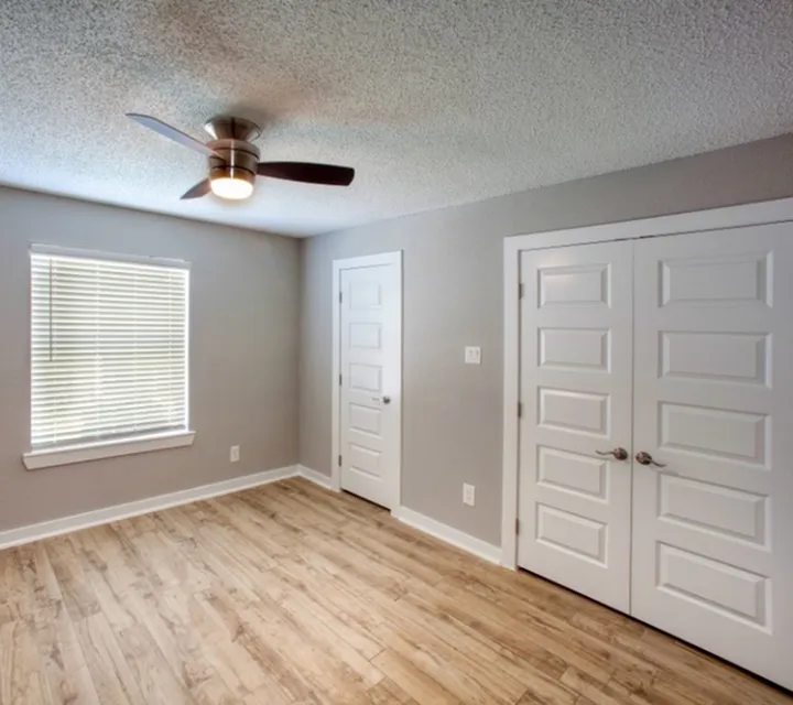 Bright and airy room featuring modern ceiling fan, elegant wood flooring, and ample closet space with stylish white doors.