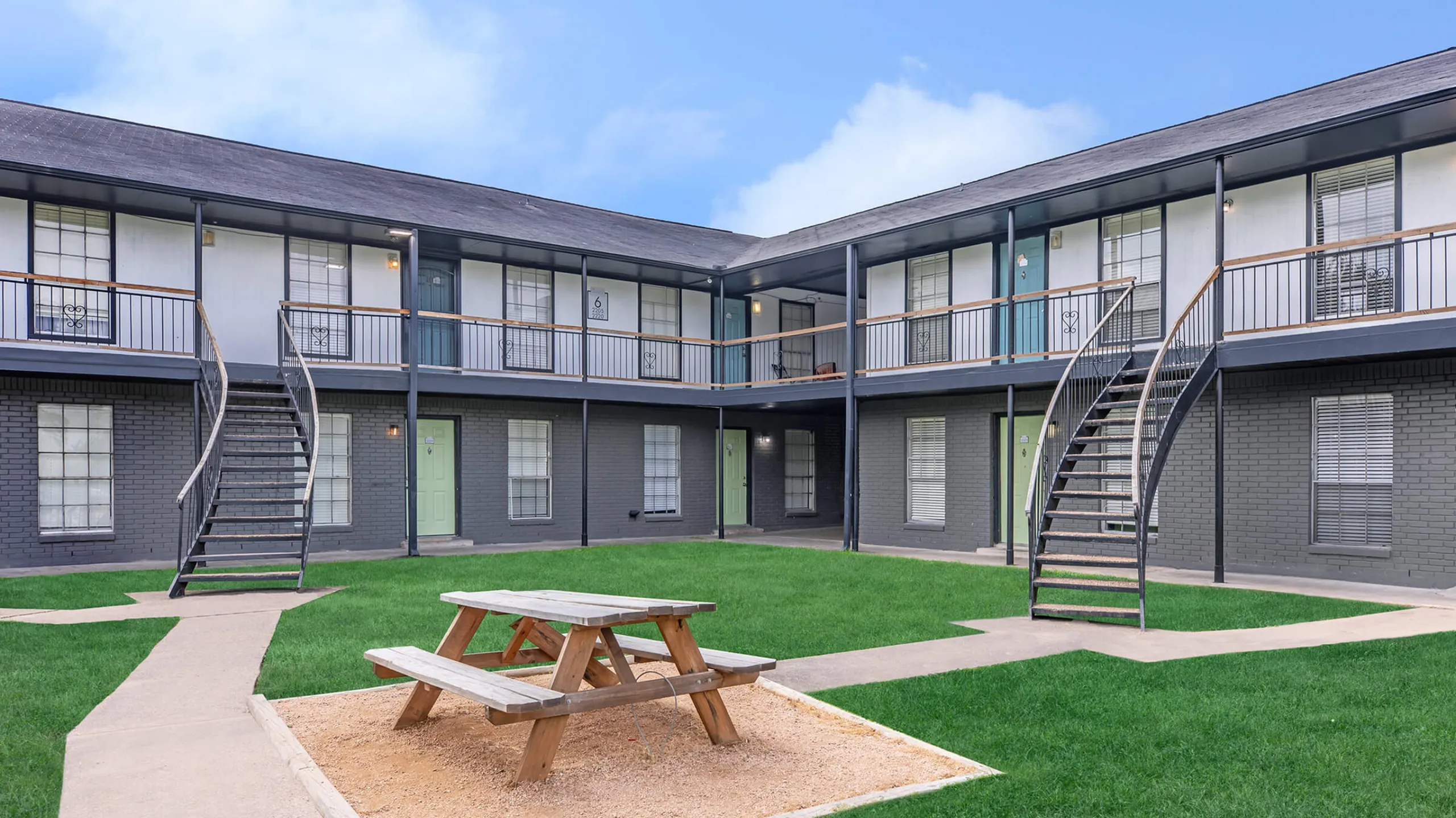 Charming two-story apartment complex with a central courtyard featuring a picnic area and lush green lawns.