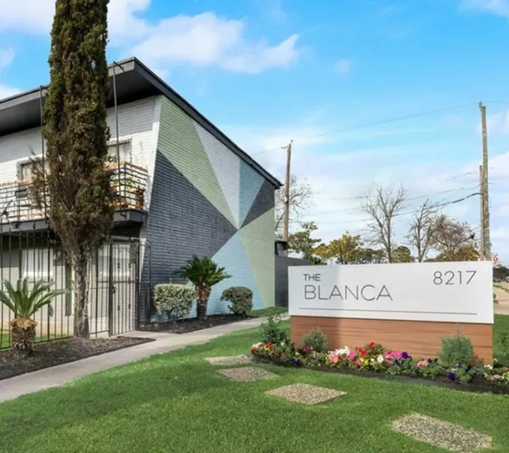 Modern apartment exterior at The Blanca with artistic geometric mural and vibrant landscaping.