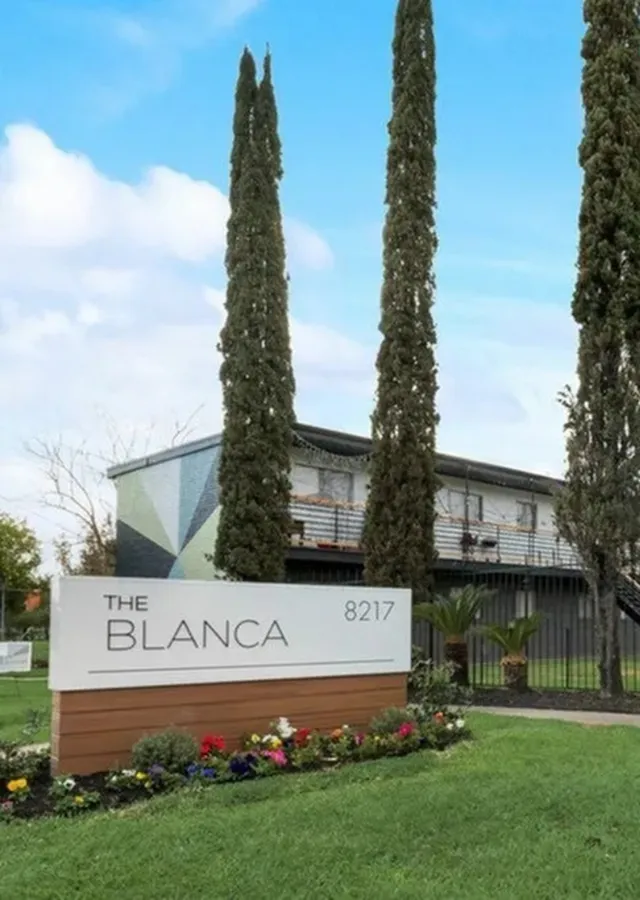 Charming apartment complex 'The Blanca' with modern facade, lush greenery, and blooming flower beds at address 8217.