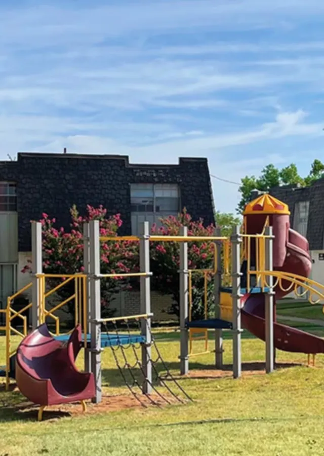 Charming apartment complex with a vibrant playground and slides amidst lush green surroundings.