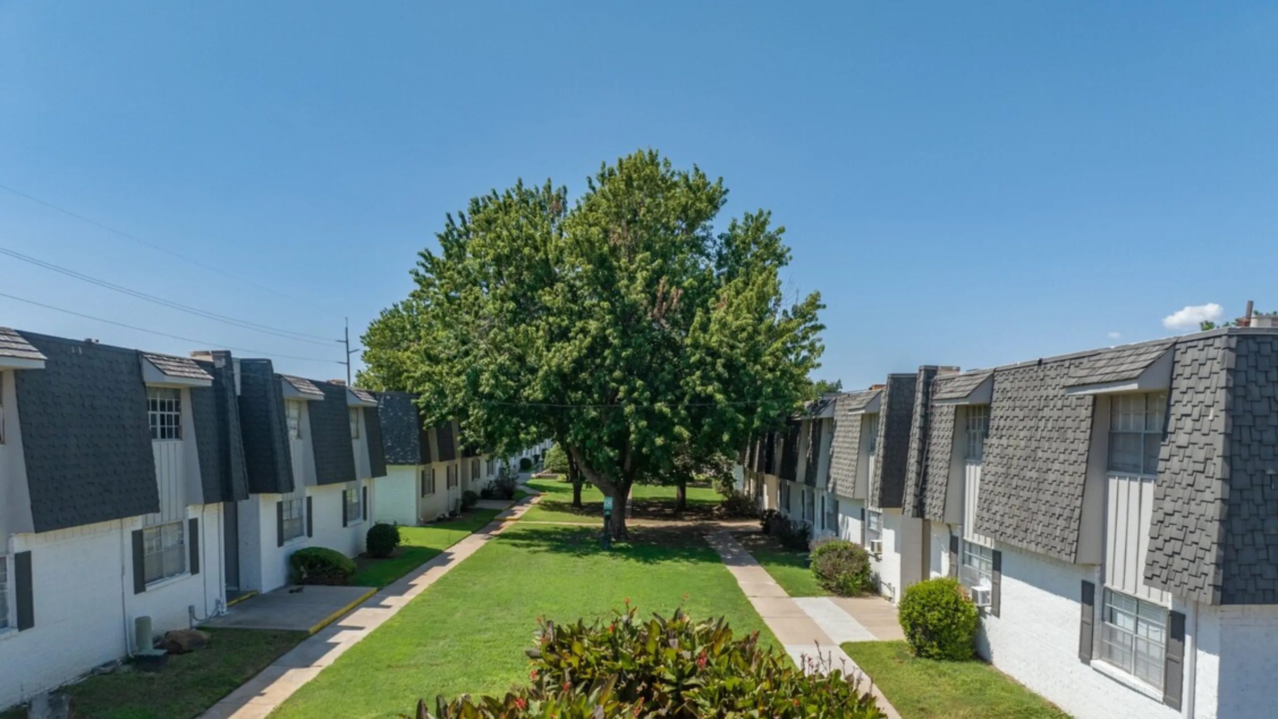 Tranquil garden walkway between charming, shingle-roofed apartment buildings, offering scenic views and abundant greenery.
