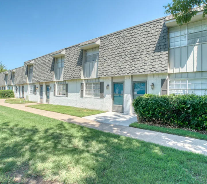 Charming townhouse exterior with textured roof, large windows, and vibrant green lawn.