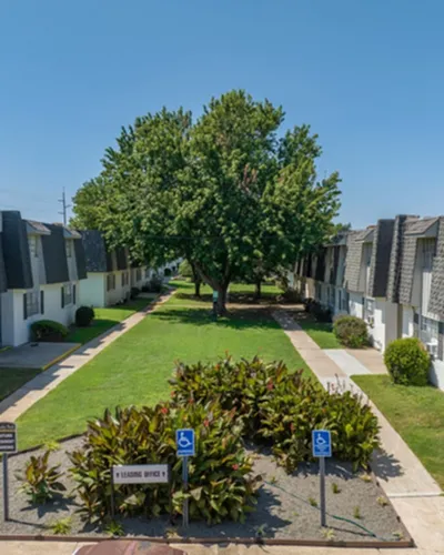 Charming apartment complex with beautiful landscaping, lush greenery, and inviting pathways under a clear blue sky, perfect for comfortable living.