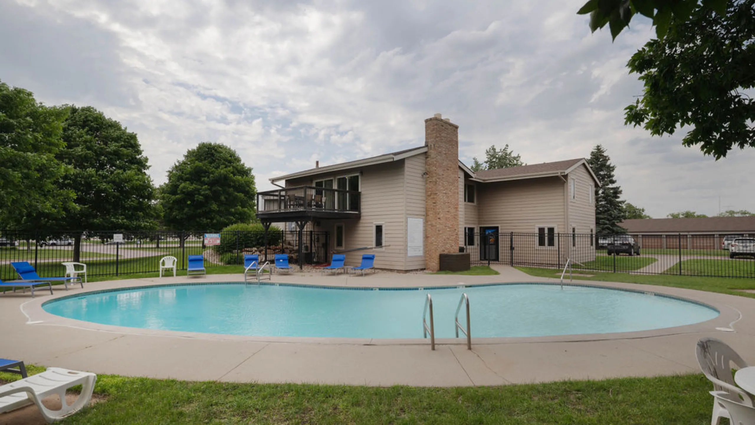 Inviting outdoor pool area with stylish lounge chairs, nestled beside a charming two-story apartment building surrounded by lush greenery.