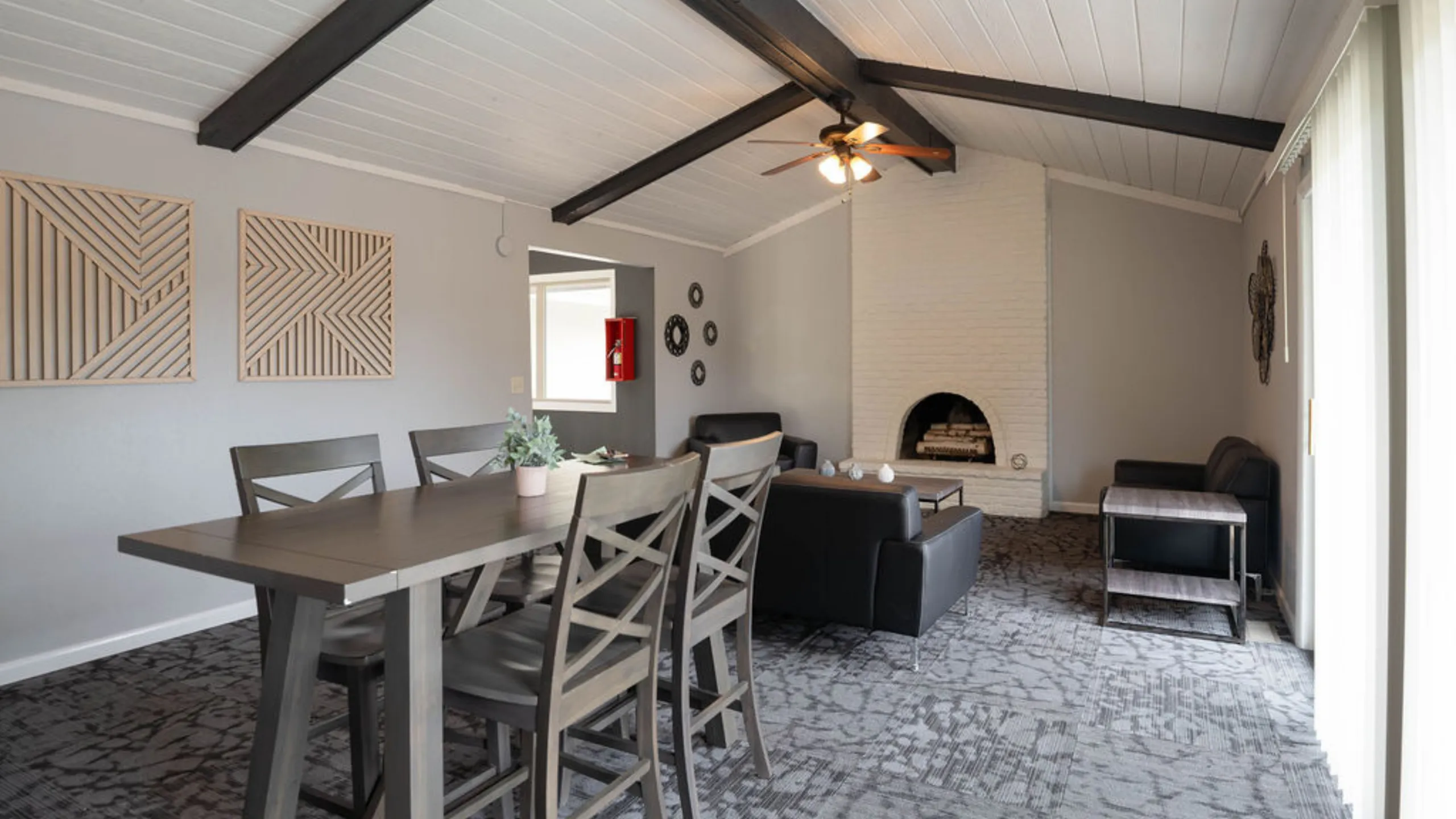 Charming living space with high ceilings, rustic wooden beams, and a cozy fireplace, featuring a sleek dining table and modern seating.