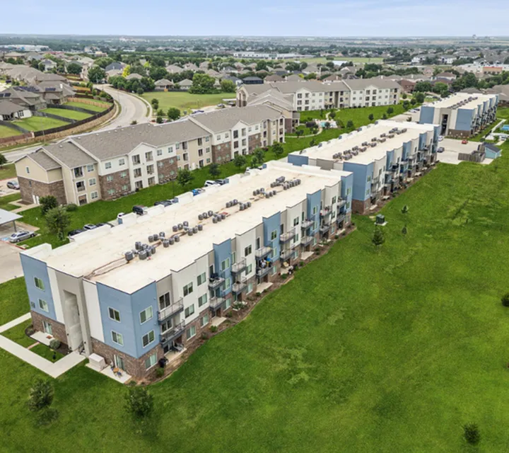 Modern apartment complex surrounded by lush greenery, featuring multiple stories with balconies and scenic views.