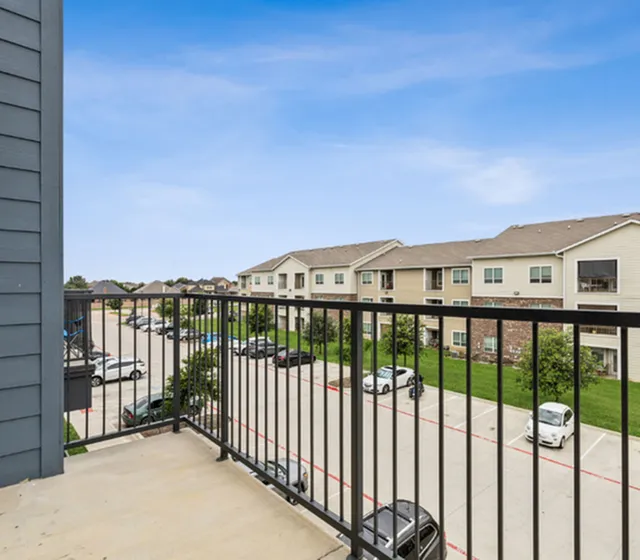 Inviting balcony view of apartment complex with blue skies and neatly lined parking area.