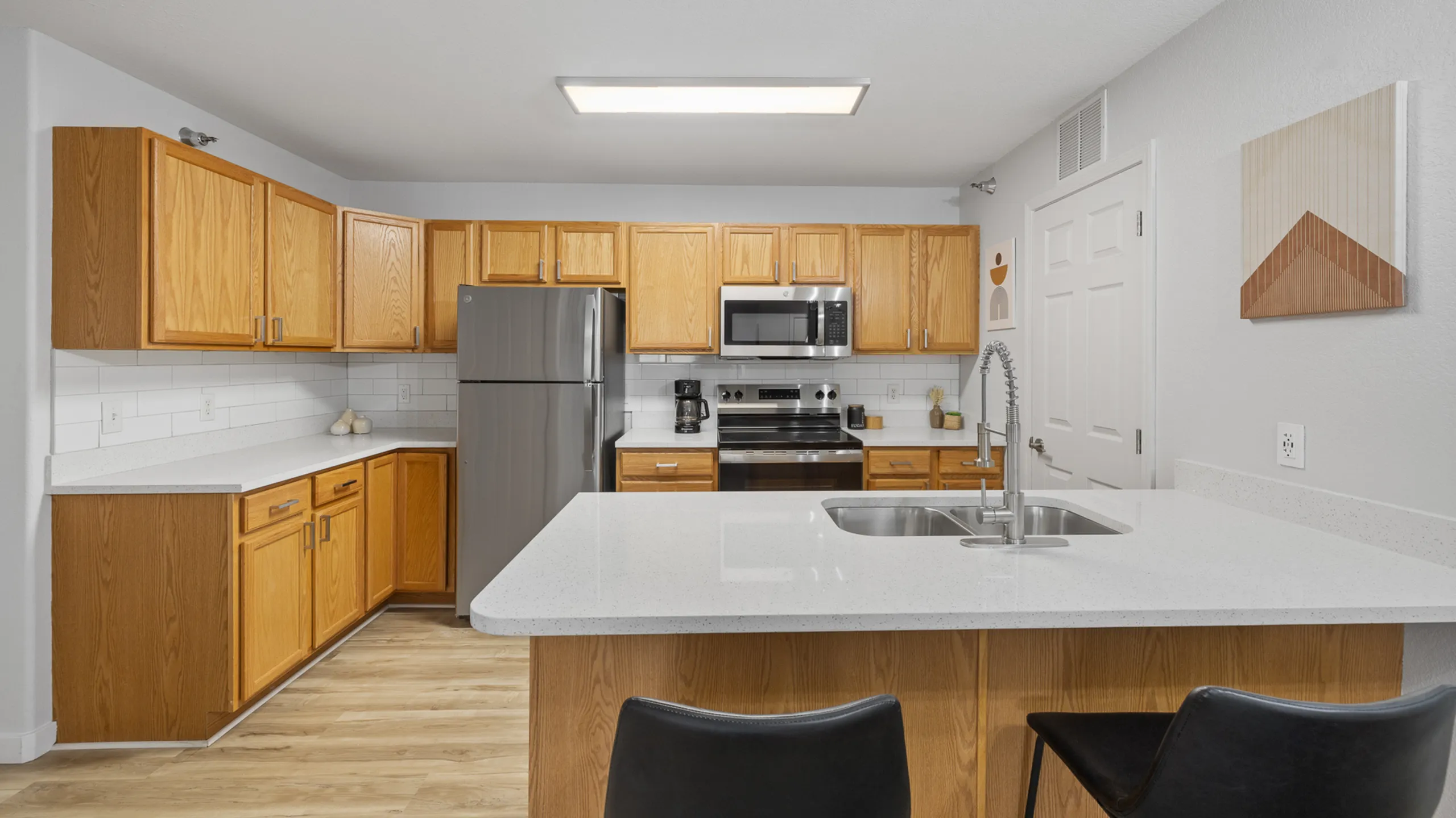 Modern kitchen with elegant oak cabinets, sleek stainless steel appliances, and a pristine white countertop breakfast bar.