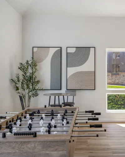 Chic recreation room with a stylish foosball table, modern art, natural light, and lush plant decor.