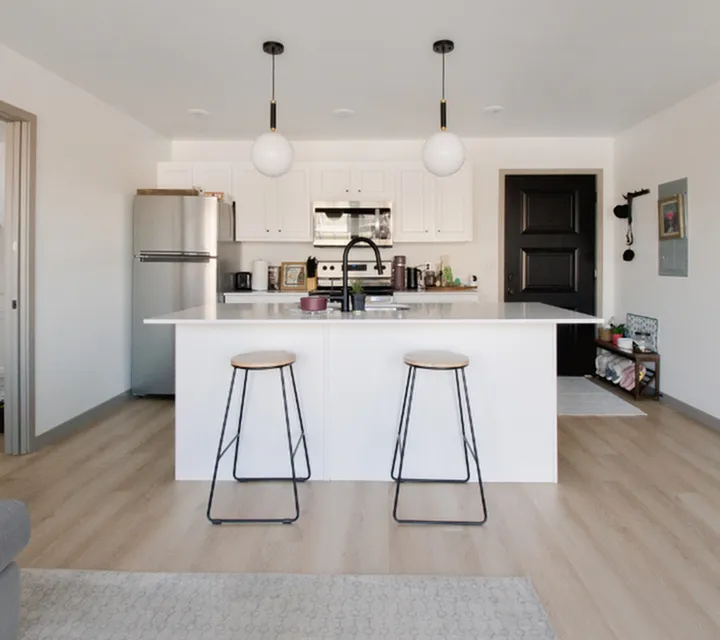Modern kitchen with sleek white cabinetry, stainless steel appliances, and a stylish island with bar seating under elegant pendant lighting.
