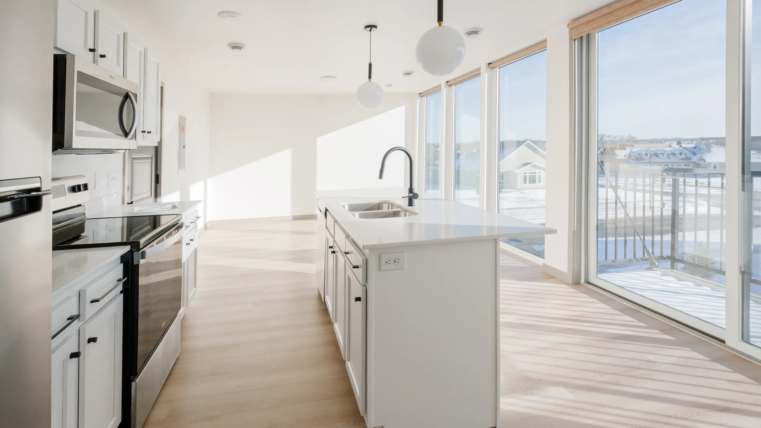 Sleek kitchen with modern appliances, expansive glass windows offering abundant natural light, and elegant wooden flooring.